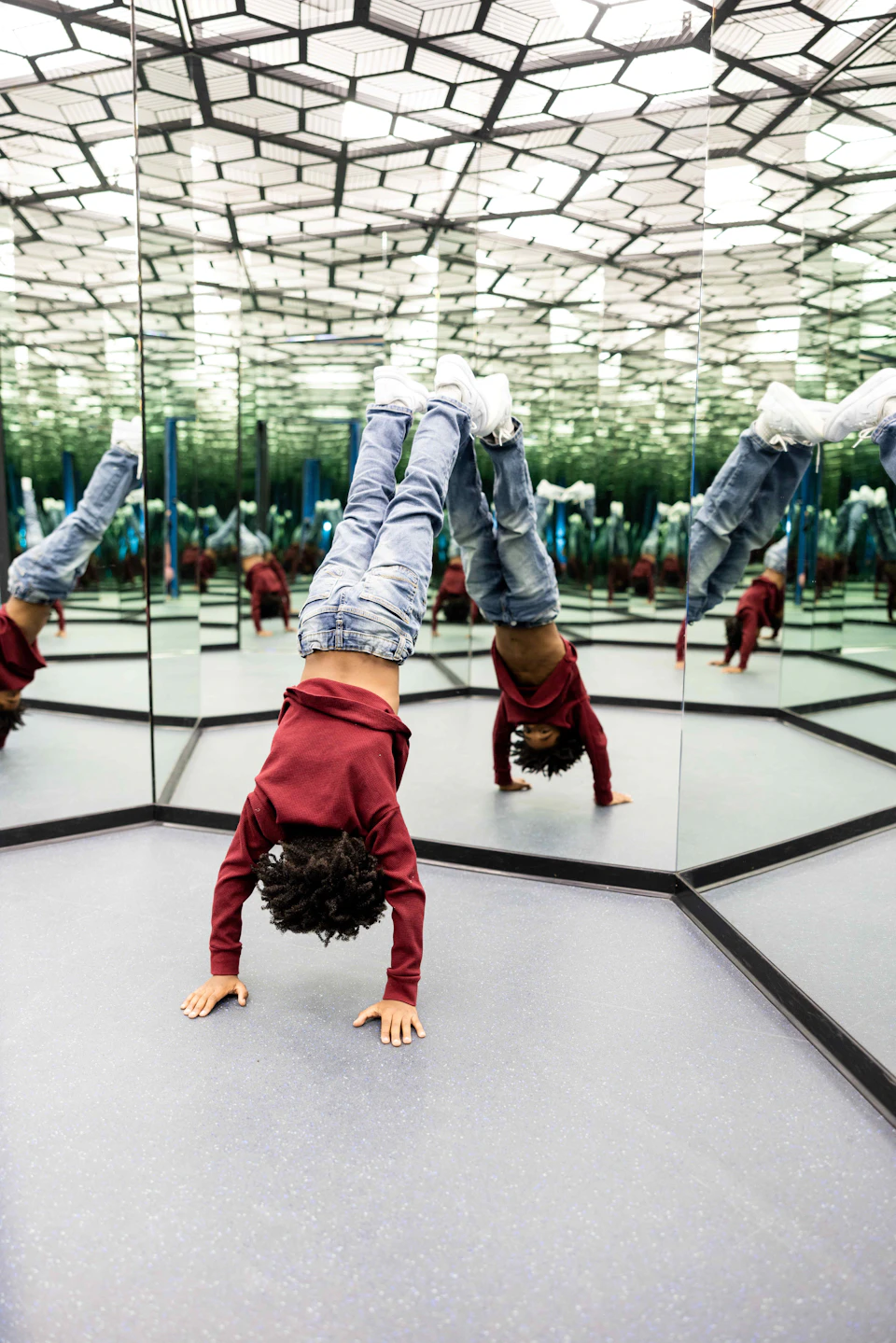 Child performing a handstand in a mirrored room, reflecting multiple angles of the pose.