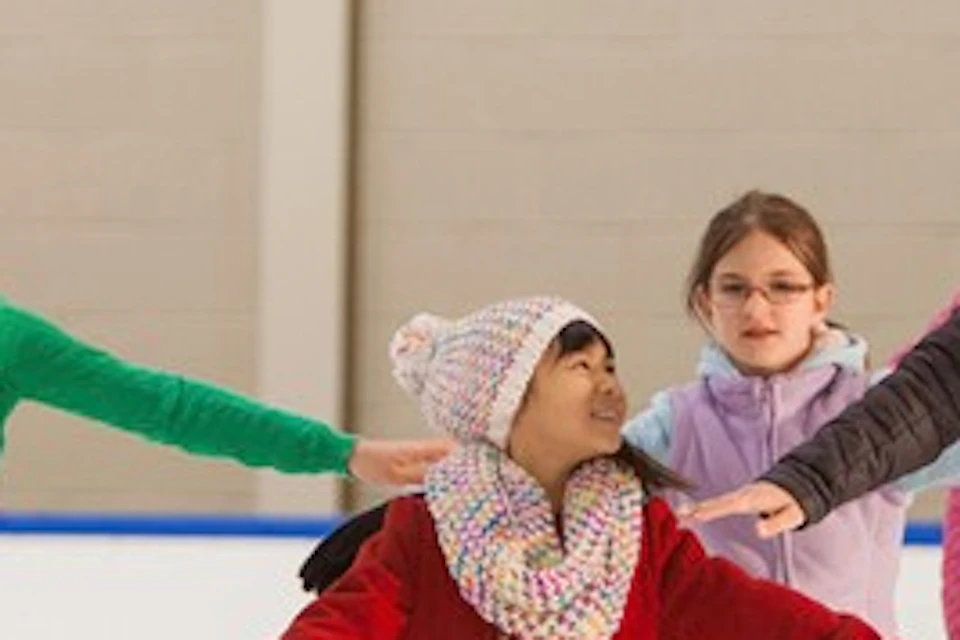 A group of children ice skating with an instructor in a skating rink, all wearing winter clothing.