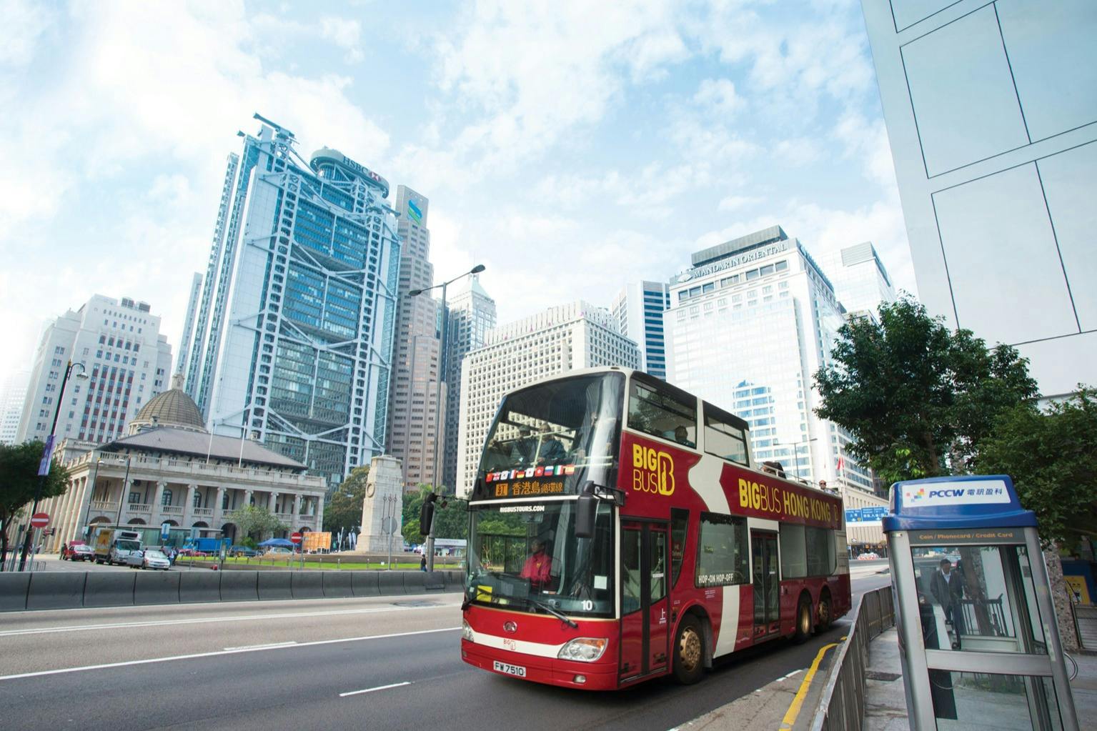 红色双层旅游巴士，标有“香港大巴士” ，坐落在城市街道上，摩天大楼现代化，背景是晴朗的天空。