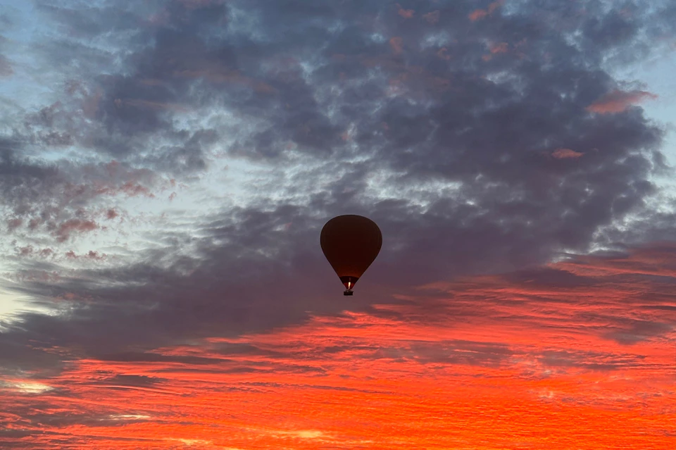 A hot air balloon silhouetted against a dramatic sky at sunset, with vivid red and orange clouds.