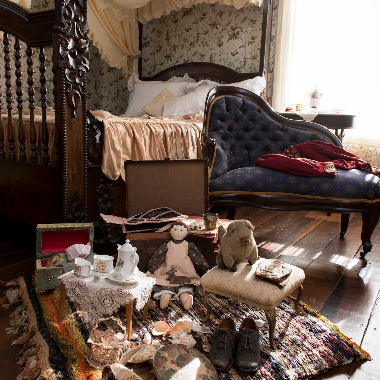 A vintage bedroom with a wooden bed, chaise lounge, toys, tea set, and scattered items on a patterned rug.