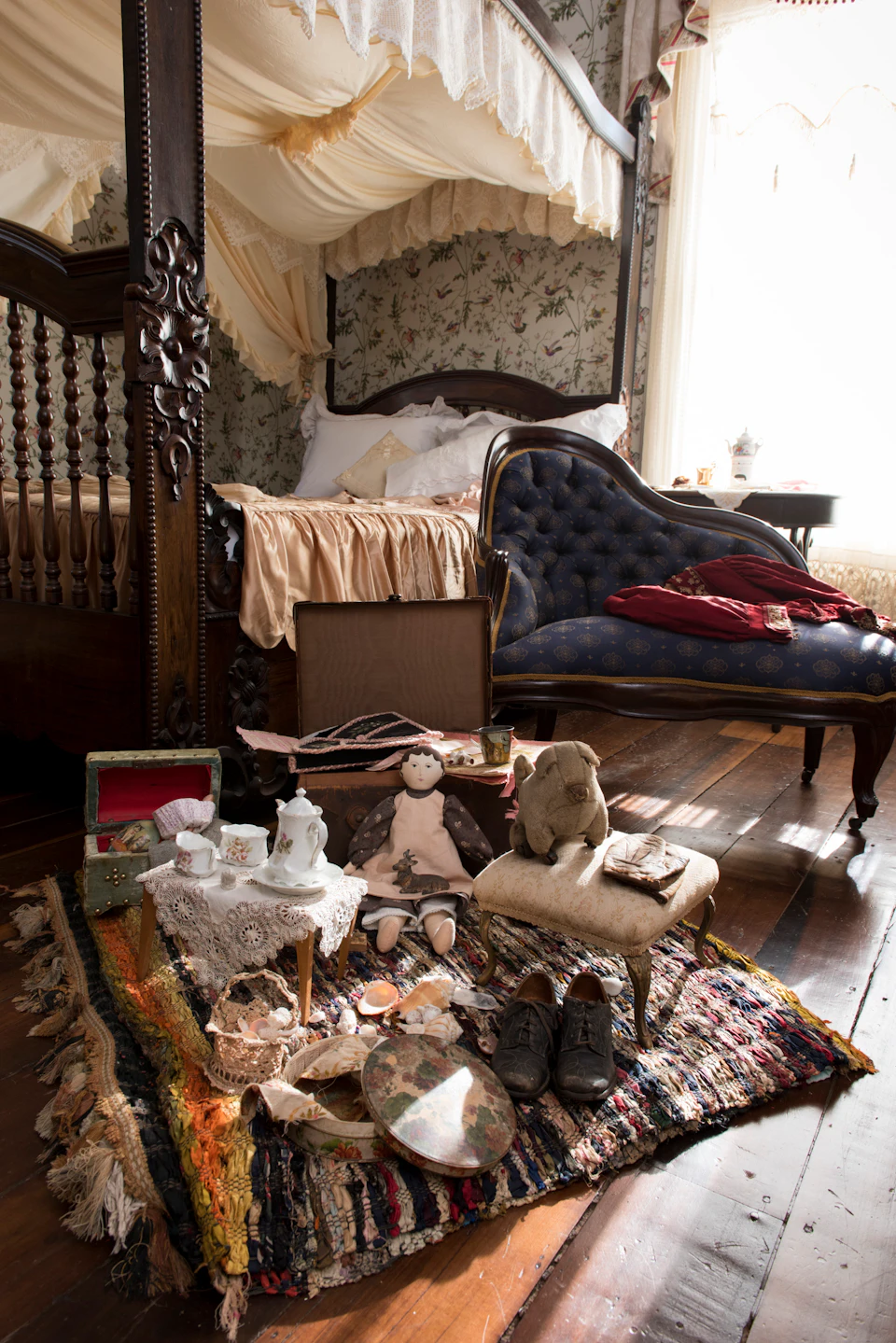 A vintage bedroom with a wooden bed, chaise lounge, toys, tea set, and scattered items on a patterned rug.