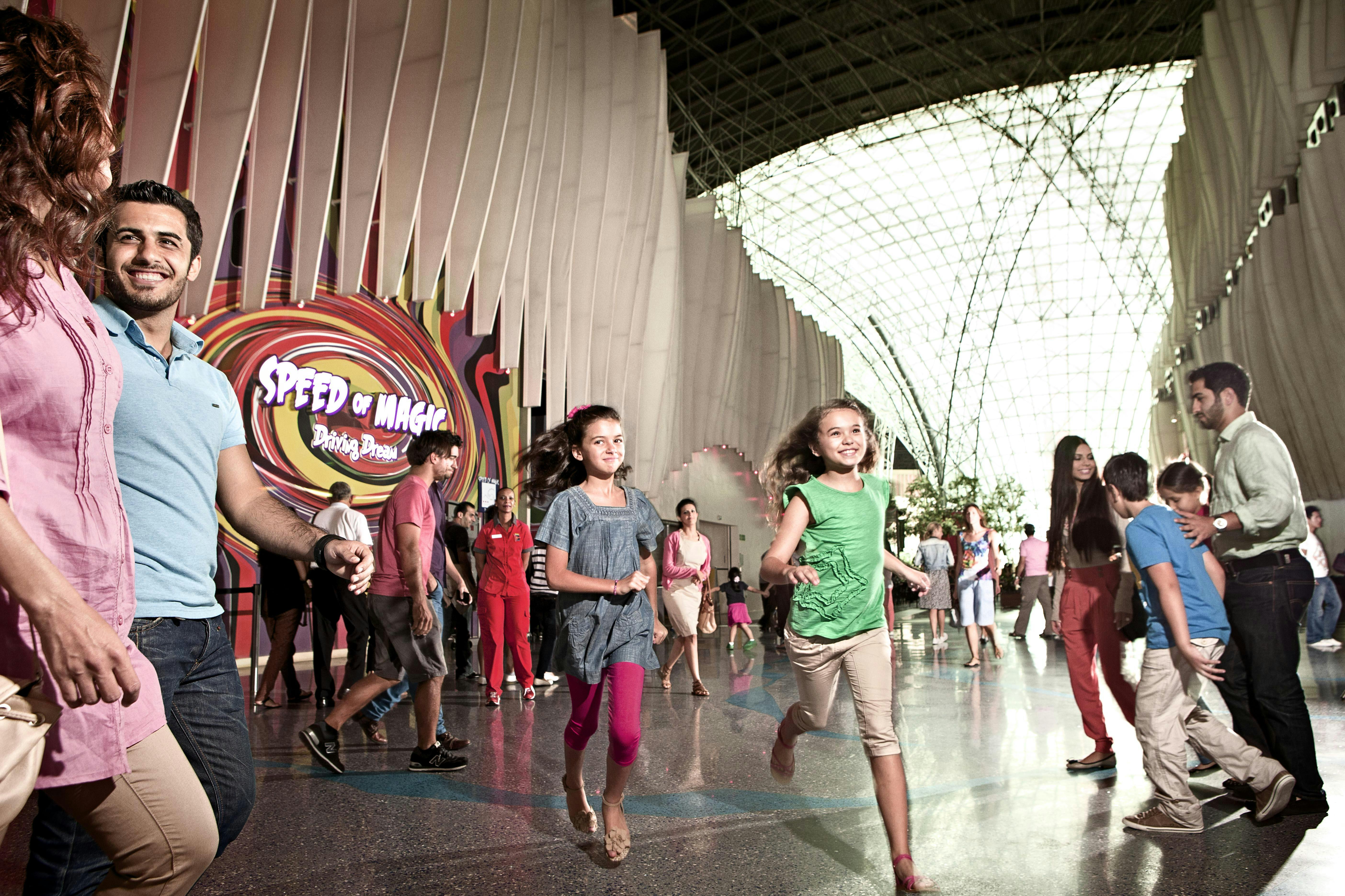 People walking and smiling inside a modern building with a colorful "Speed of Magic" sign on the wall.