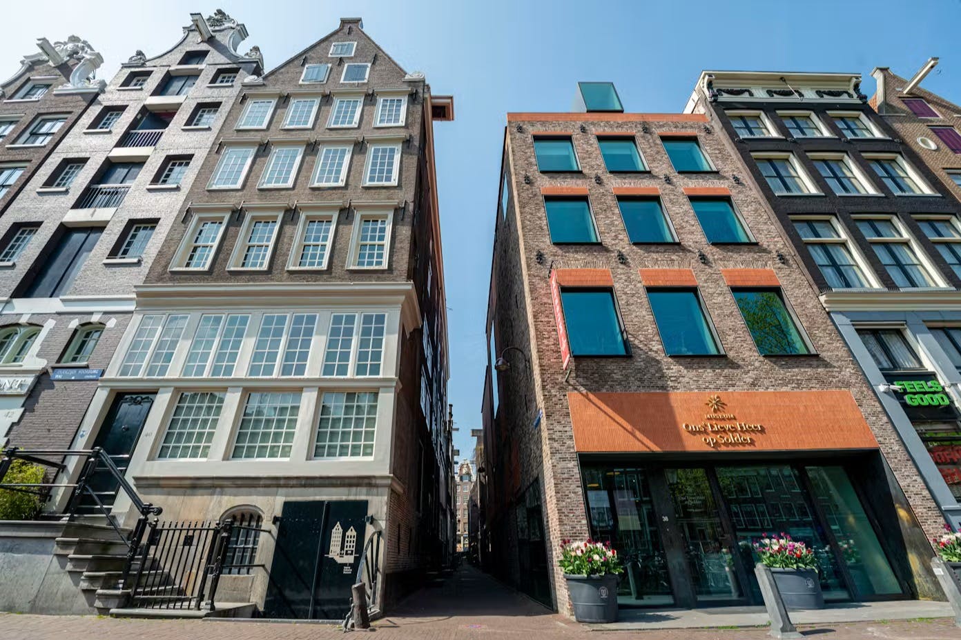 Um beco estreito entre dois edifícios, um histórico com janelas de caixilhos brancos e o outro moderno com detalhes em laranja.