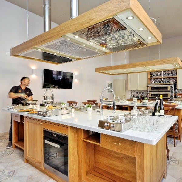 Μια ευρύχωρη μοντέρνα κουζίνα με δύο πάγκους νησιών, μαγειρική εστία, διάφορα είδη μαγειρικής και ένα άτομο που ετοιμάζει φαγητό.