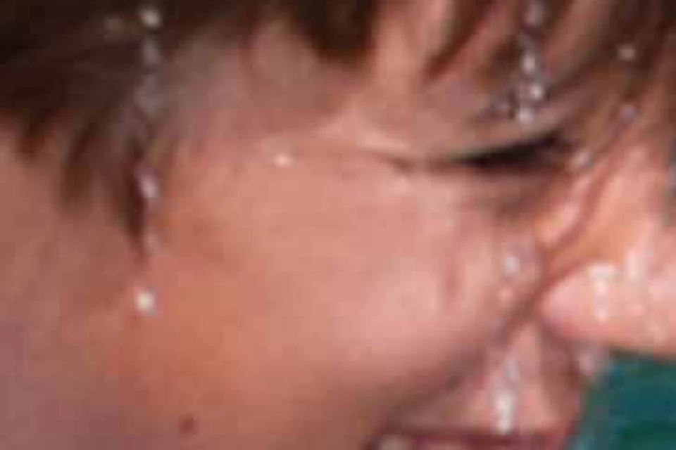 A boy wearing a life vest interacts joyfully with a dolphin in clear, shallow water.