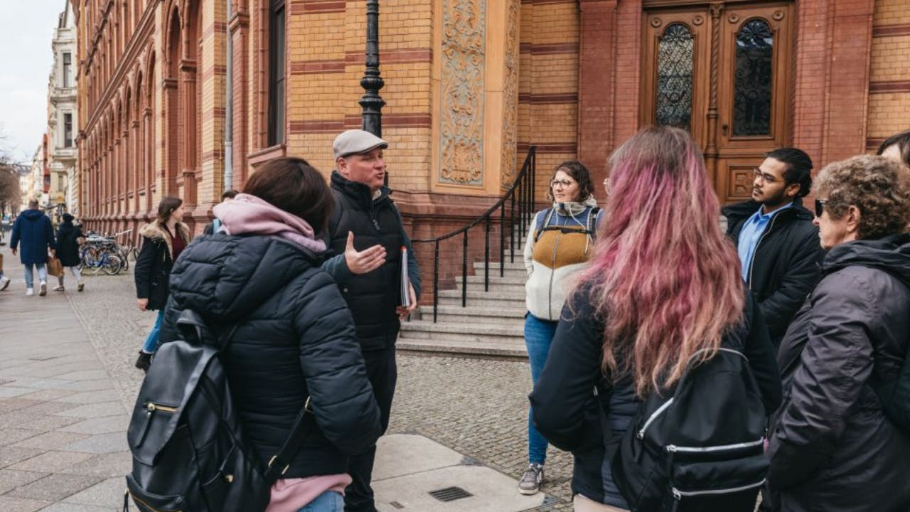People in outdoor clothing gathered in front of a historic building with ornate doors and a staircase.
