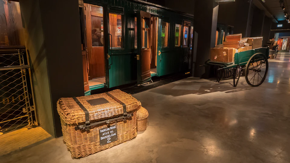 A vintage train car next to a stack of old-fashioned wicker luggage with a label reading "BRUSSEL ZUID."