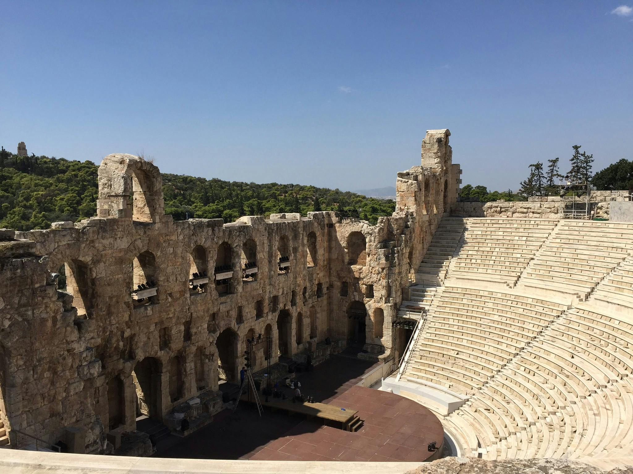 En uråldrig stenamfiteater med sittplatser och delvis förstörda väggar under en klarblå himmel med träd i bakgrunden.