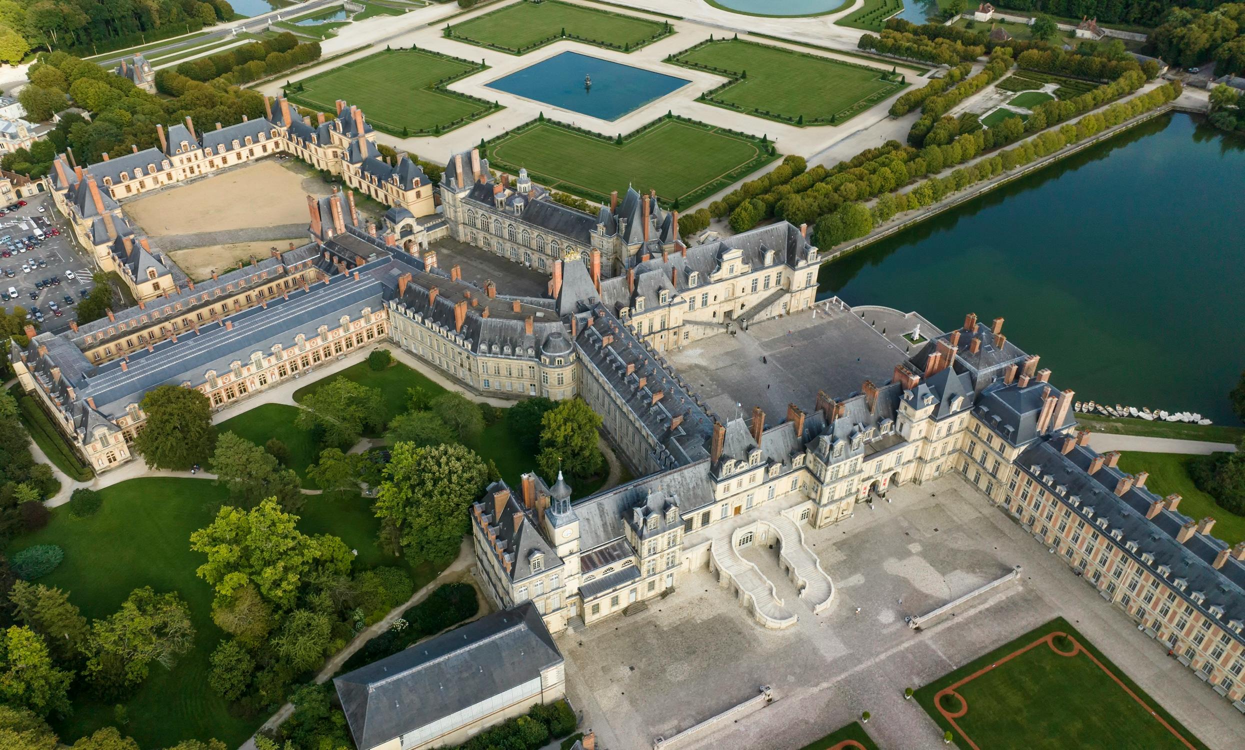 Aerial view of an ornate historical chateau with extensive gardens and symmetrical water features.