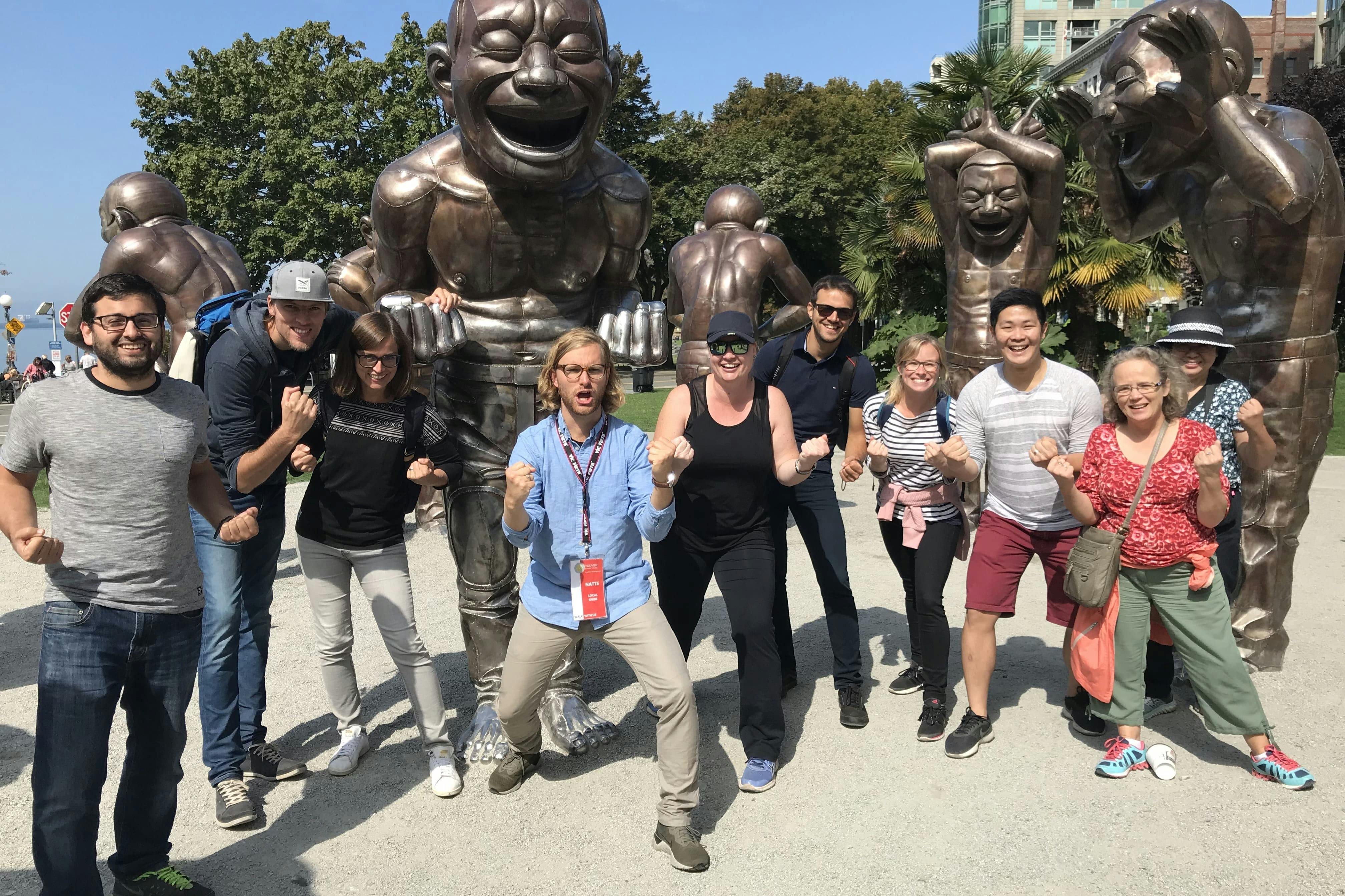 Skupina lidí, kteří za slunečného dne nadšeně pózují před velkými bronzovými sochami v parku.