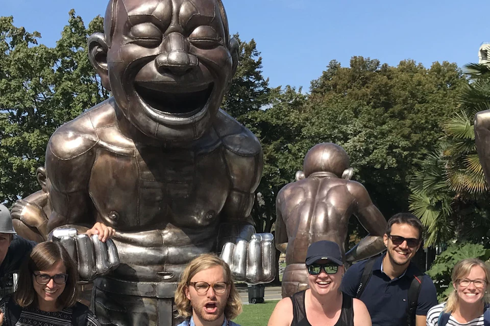 A group of people posing enthusiastically in front of large bronze statues in a park on a sunny day.