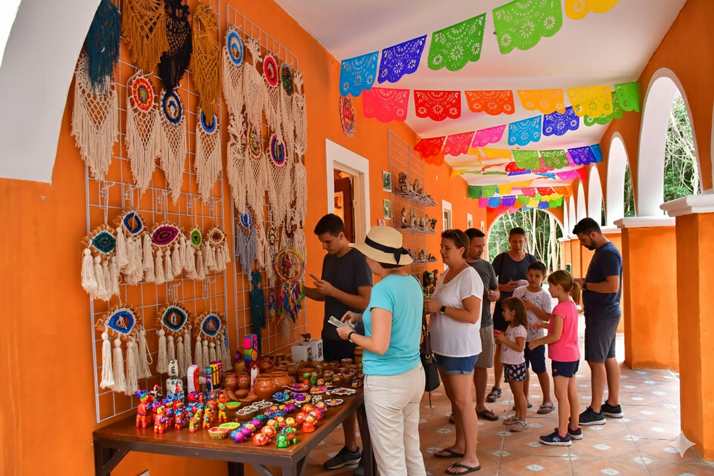 People browsing colorful crafts and souvenirs under a decorated corridor with vibrant papel picado banners.