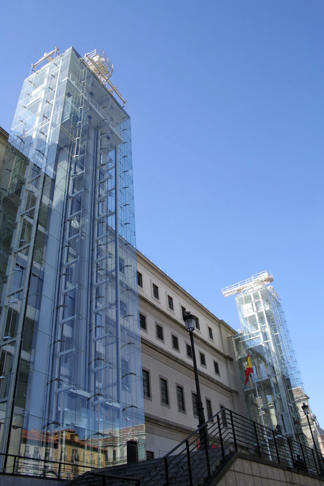 Glass elevator towers attached to a beige building with multiple windows under a clear blue sky.