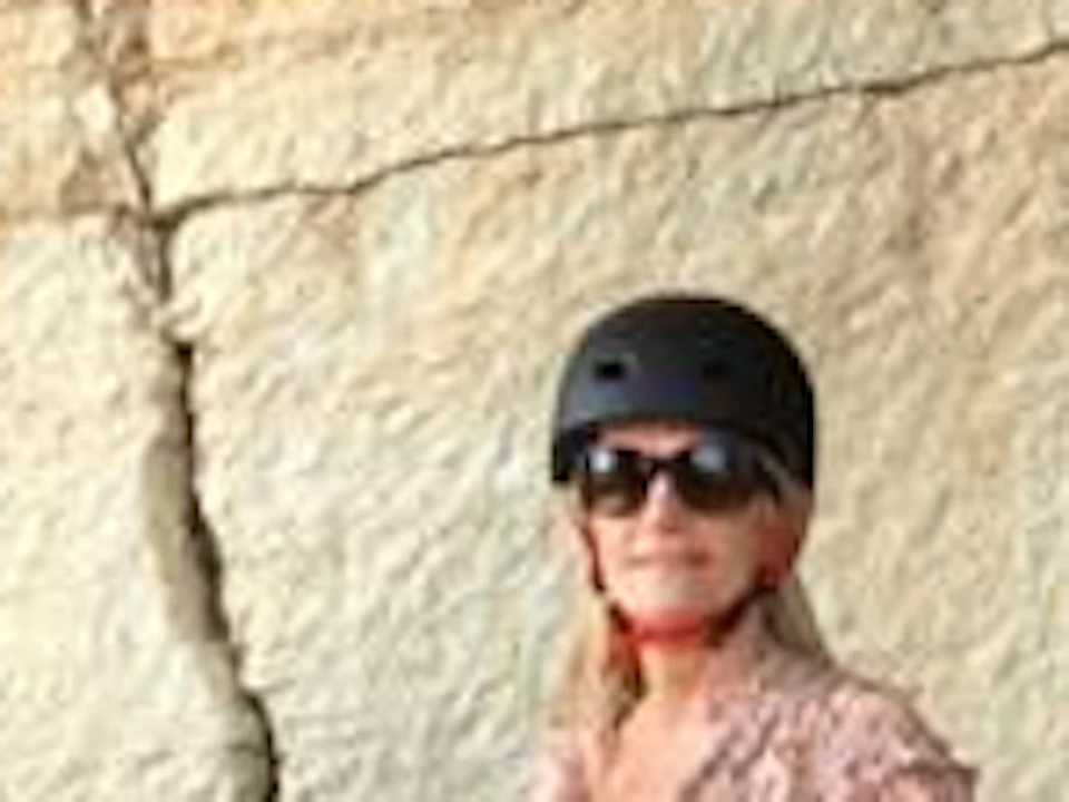 Four people with bicycles stand in front of large rock formations, wearing helmets and casual clothing.