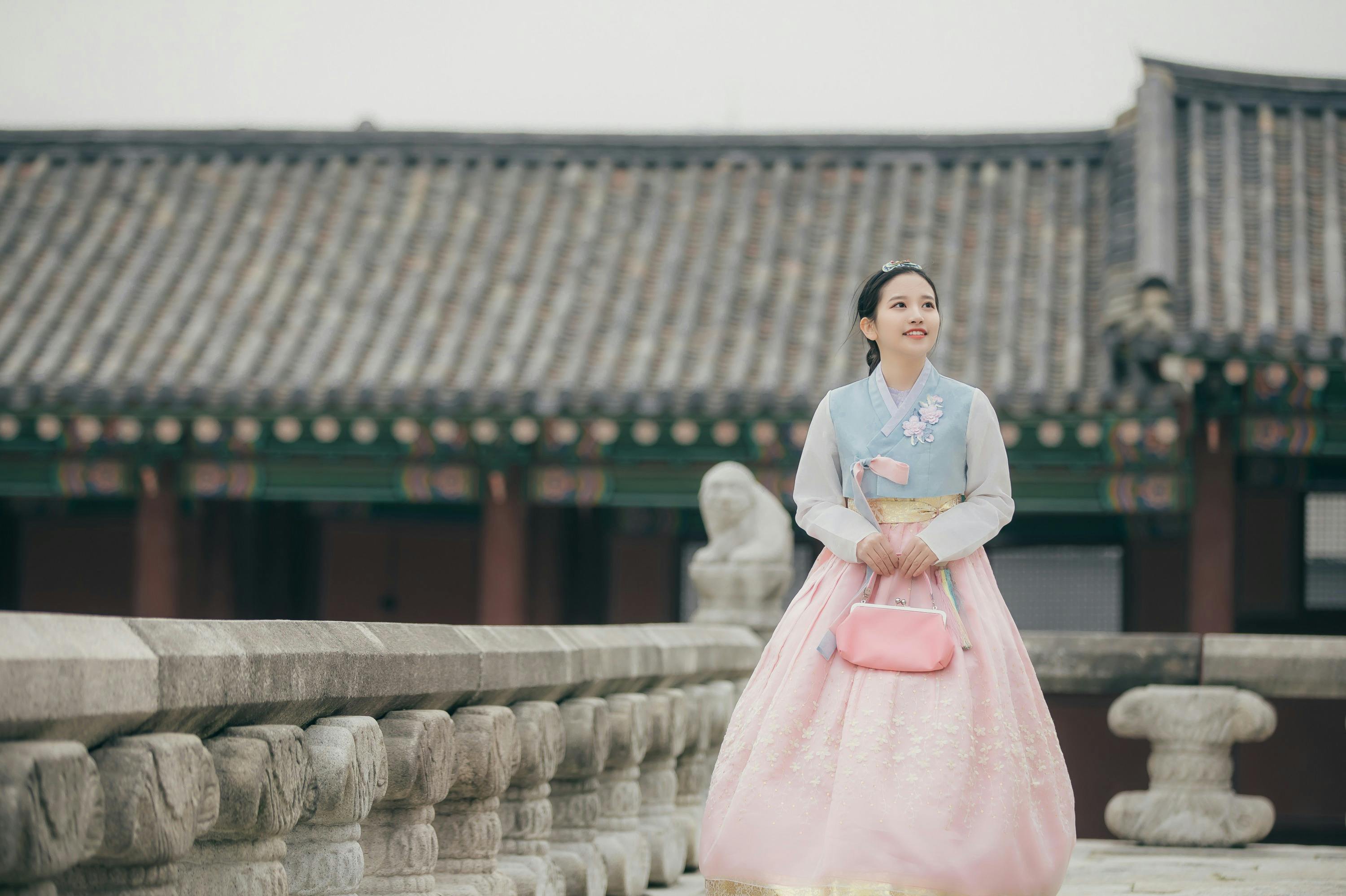 A person in traditional attire stands on a stone bridge in front of a historic building with tiled roofs.