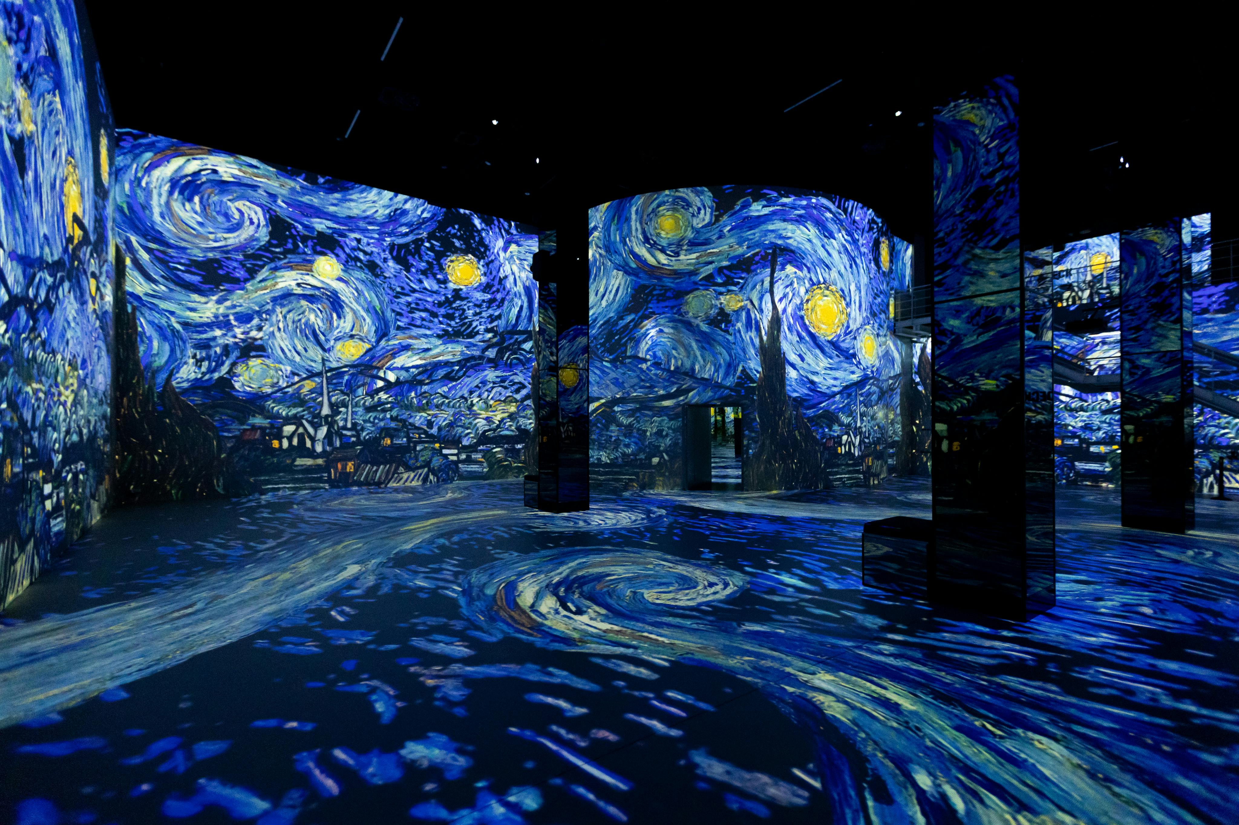 Room illuminated with projections of Van Gogh's "Starry Night" on walls and floor, creating an immersive art experience.