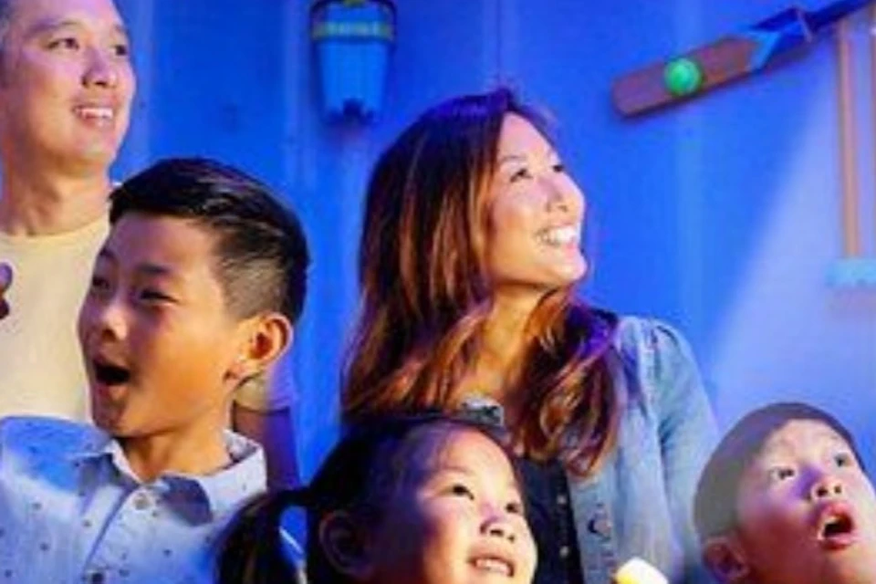 A group of five people, including children and adults, holding light-up objects in a colorful room with a stop sign on the wall.