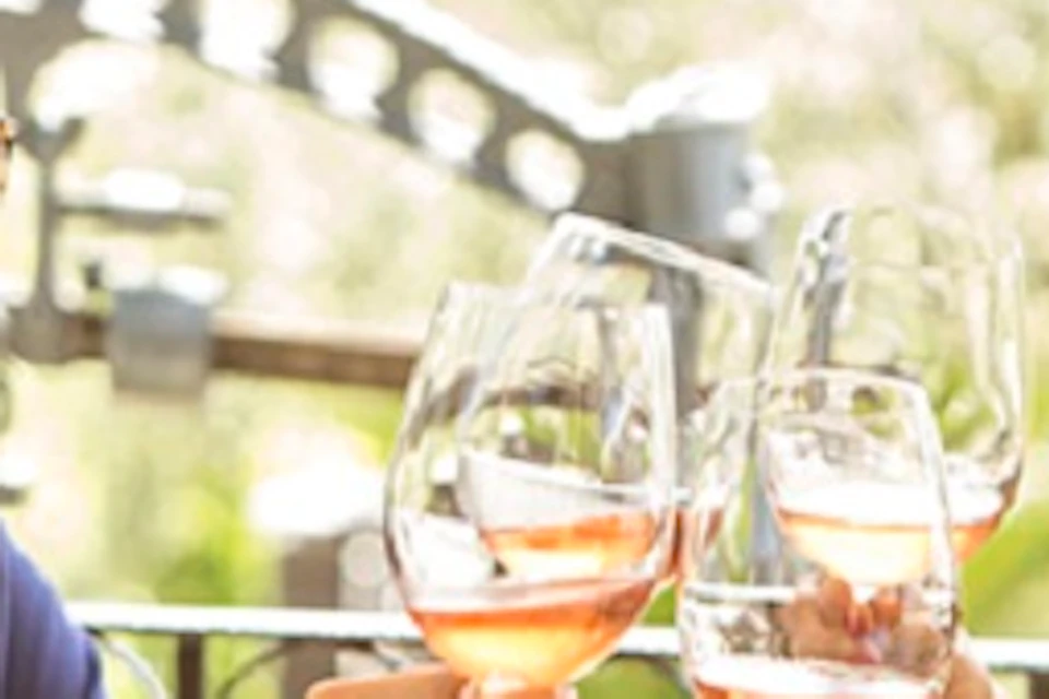 Three people toast with wine glasses around a table with food at an outdoor dining area, all smiling and enjoying each other’s company.
