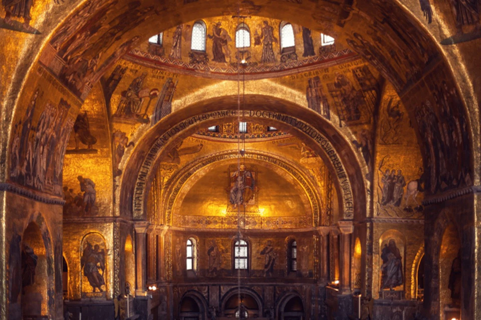 Interior of a cathedral with golden mosaics and arched ceilings, featuring religious artwork and intricate details.