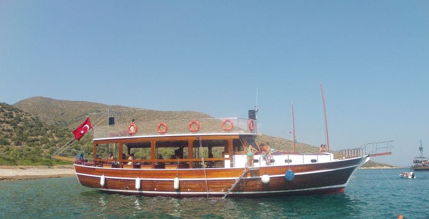 바위 언덕 근처에 정박한 상부 갑판에 구조대가 있는 나무 보트로, 사람들은 맑고 푸른 하늘 아래에서 편안한 휴식을 취하고 있습니다.