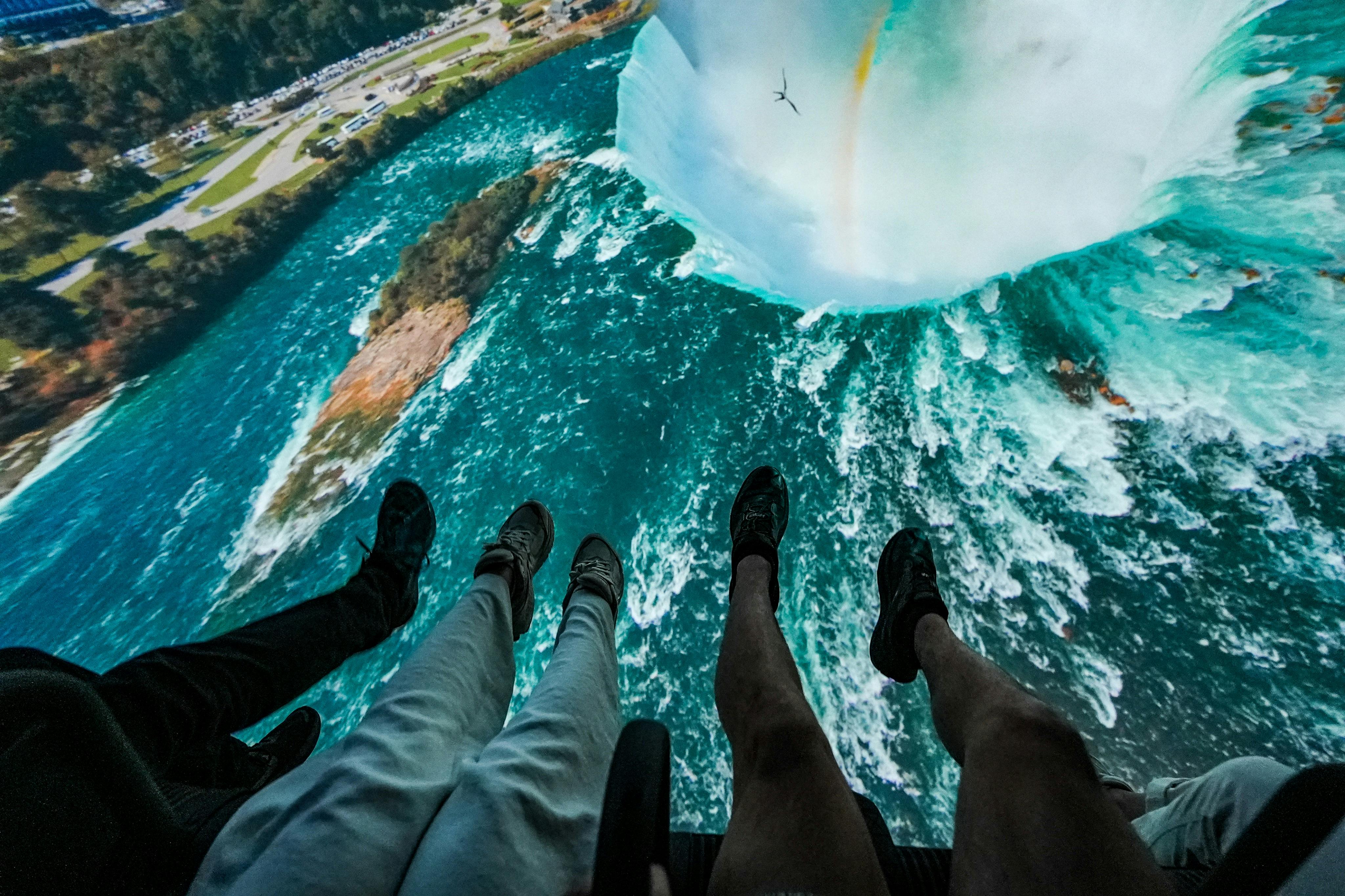 从高处看，人们的双腿悬挂在彩虹般的大瀑布上方。