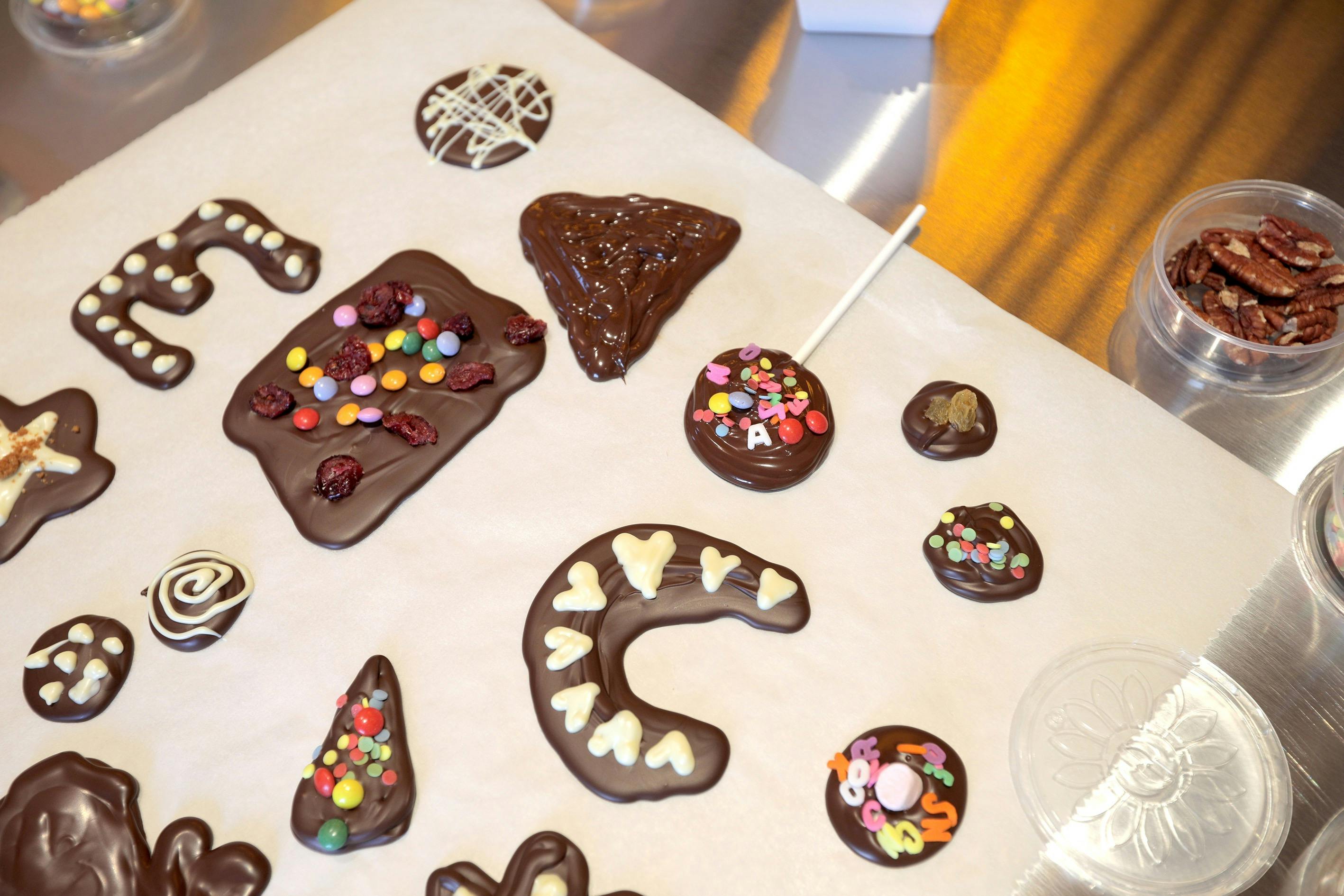 Assorted chocolate shapes decorated with colorful candies and dried fruits on a parchment paper.