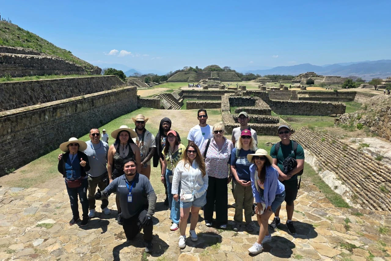 A group of people posing together outdoors at an ancient archaeological site with stone structures and a clear blue sky.