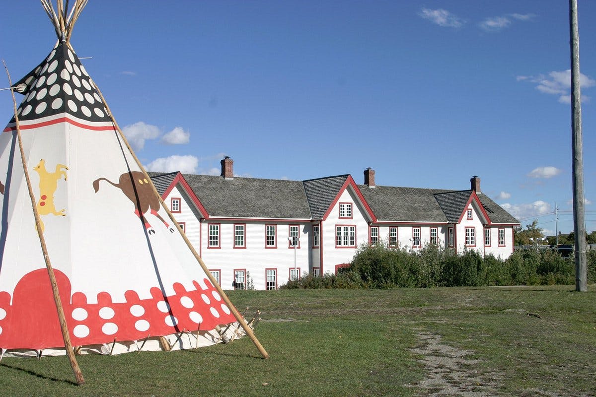 A decorated tent stands on a grassy field with a large, multi-story white building with red trim in the background under a clear blue sky.