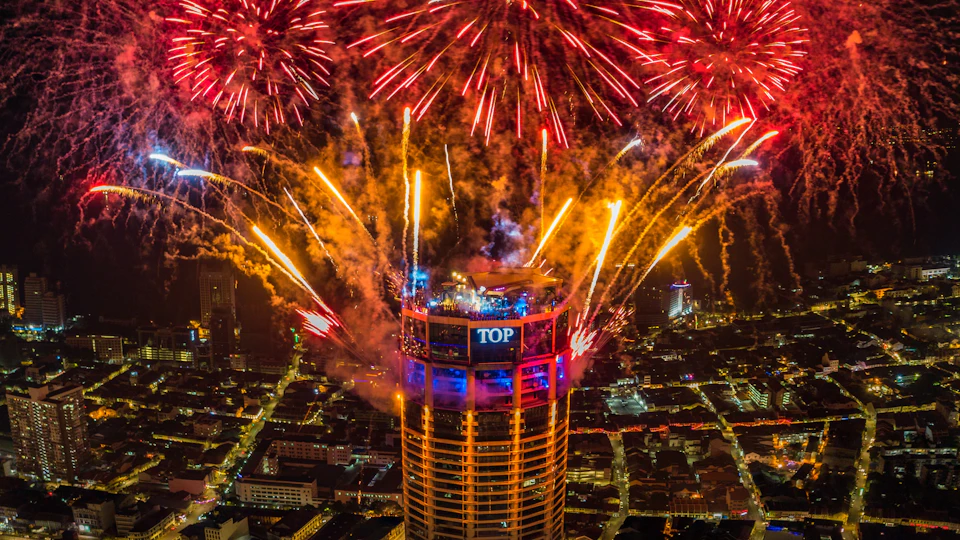 A tall building with the word 'TOP' on it is surrounded by vibrant fireworks at night over a cityscape.