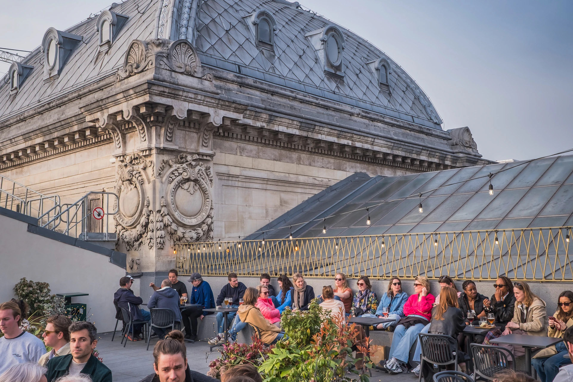 People seated on a rooftop terrace with decorative building architecture in the background, enjoying food and conversation.
