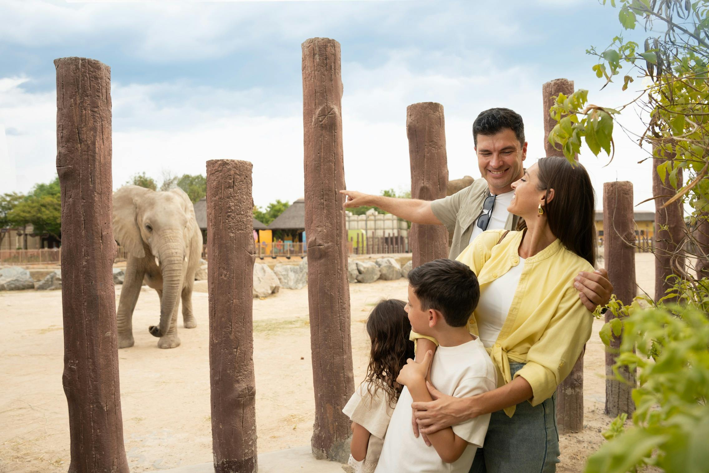 Μια τετραμελής οικογένεια απολαμβάνει έναν εξωτερικό χώρο με ξύλινους στύλους και πράσινο κάτω από έναν συννεφιασμένο ουρανό. Ο πατέρας δείχνει κάτι από μακριά.