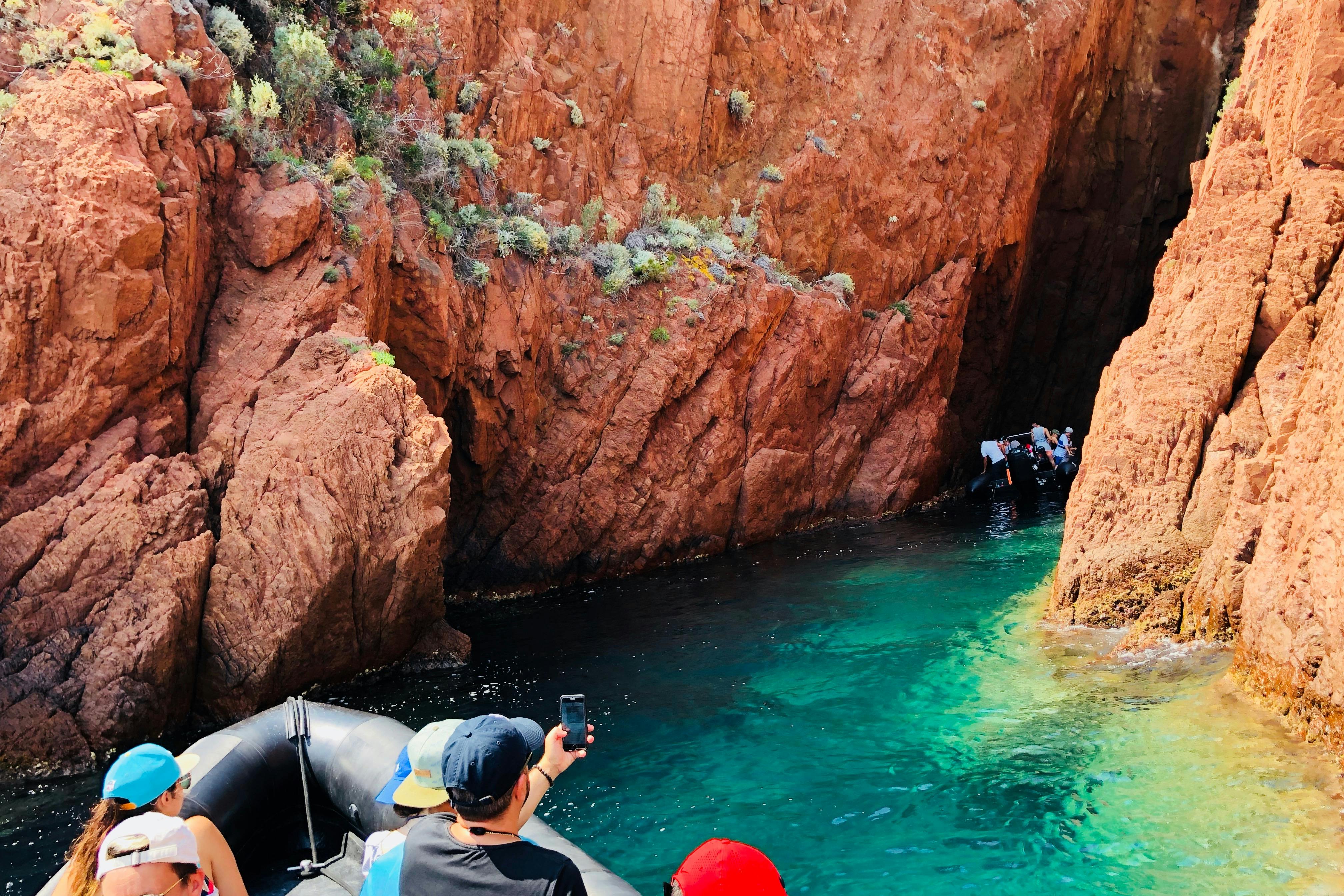 人们坐在峡谷中的船上，清澈的绿松石色海水和覆盖着稀疏植被的岩石质地墙壁。