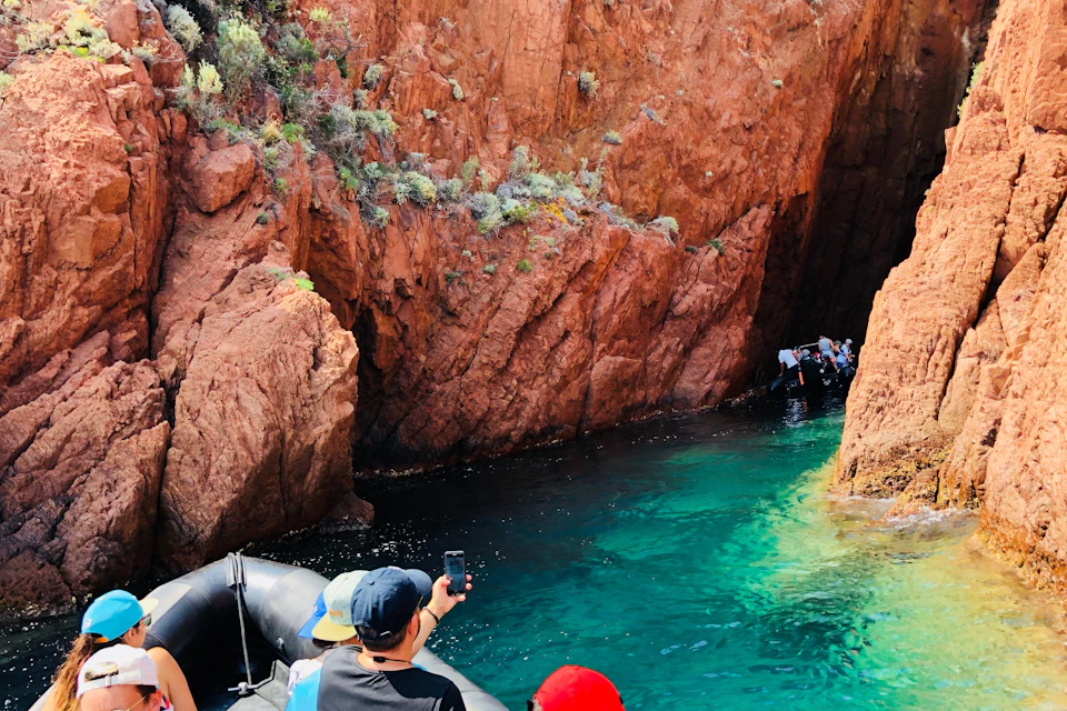 People on a boat in a canyon with clear turquoise water and rocky, textured walls covered in sparse vegetation.