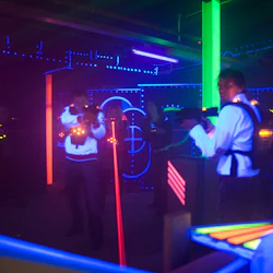 Människor som spelar lasertagg i en mörk, neonbelyst arena med glödande västar och laserpistoler.