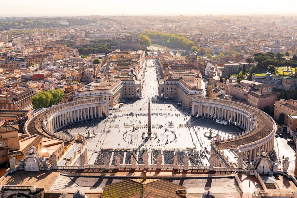 Aerial view of St. Peter's Square in Vatican City, featuring the large open plaza, central obelisk, and surrounding colonnades.