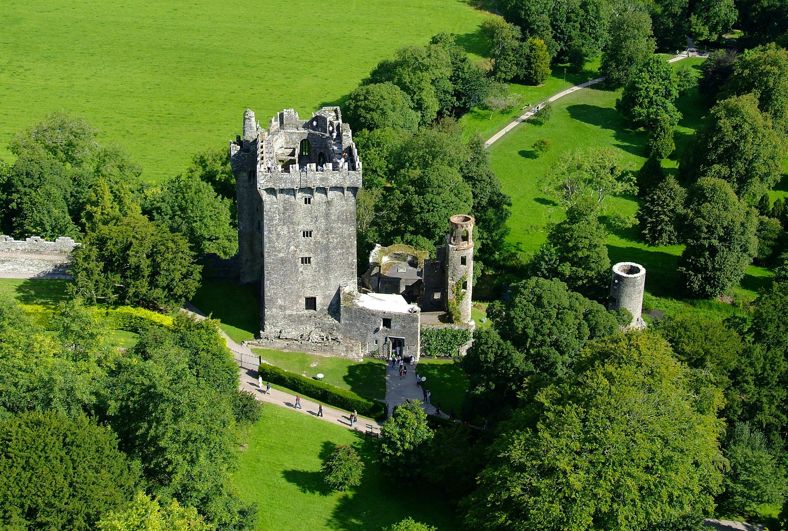 鸟瞰一座古老的石头城堡，周围环绕着郁郁葱葱的绿树和小径。