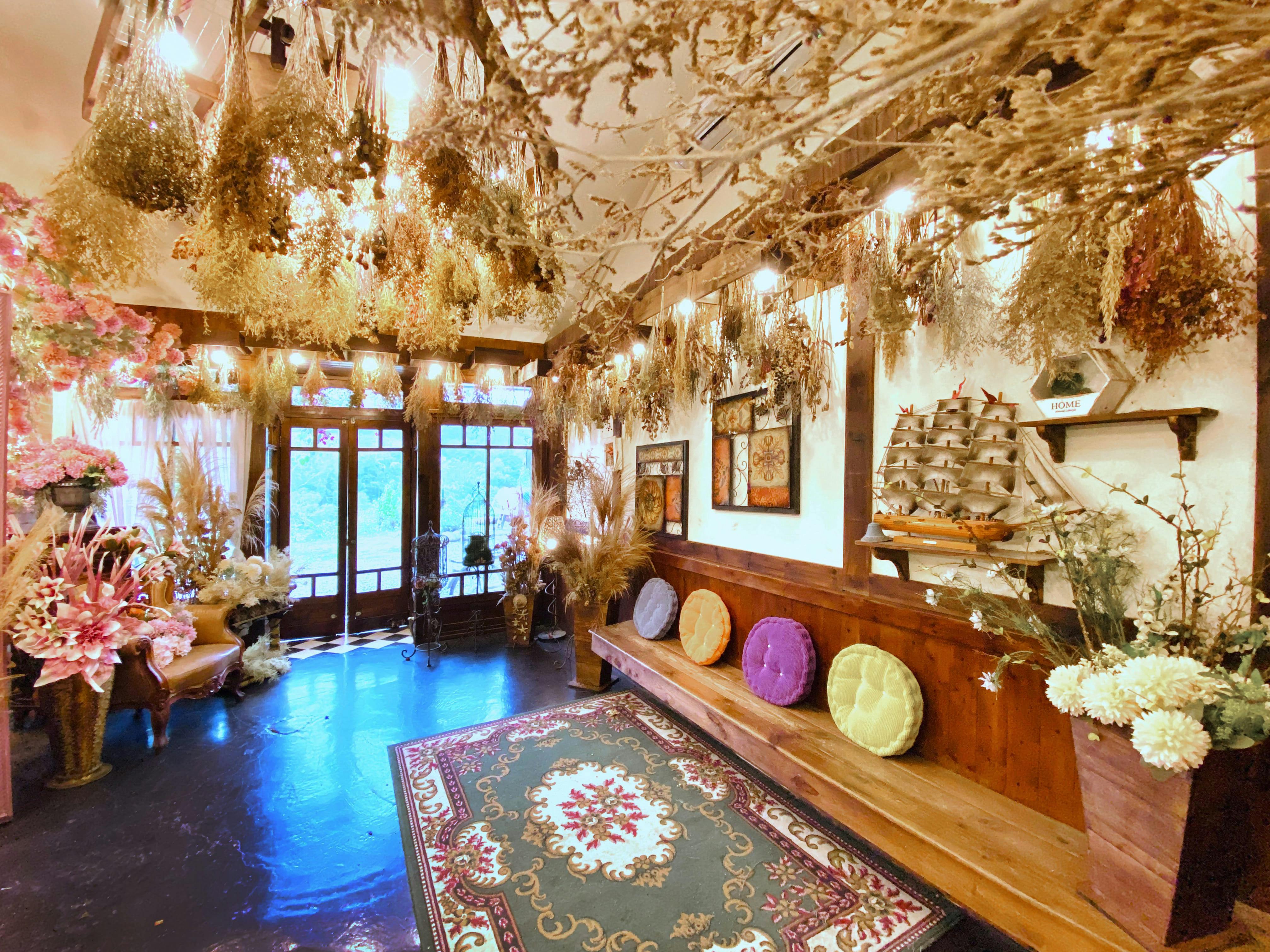 A cozy room with hanging dried plants, colorful cushions on a wooden bench, and decorative items on shelves and walls.