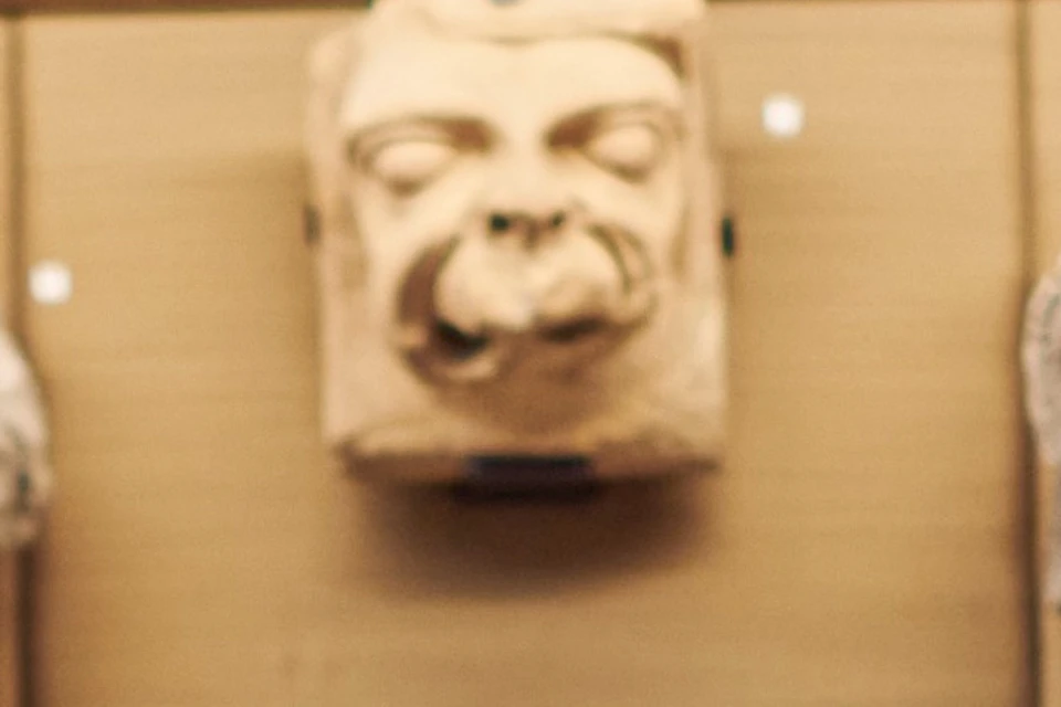 A person sitting on a bench facing a museum display of carved stone faces and sculptures mounted on a wooden background.