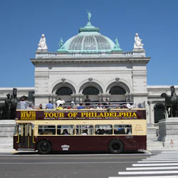 An open-top tour bus labeled "Tour of Philadelphia" in front of a historic domed building with statues.