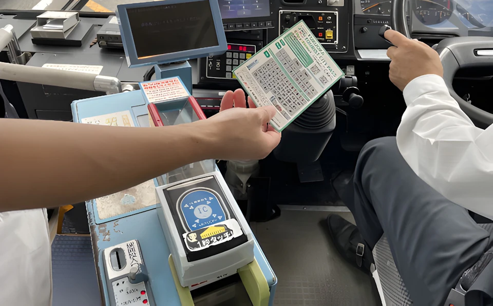A person handing a fare card to a driver inside a vehicle cockpit with control panels and a payment scanner visible.