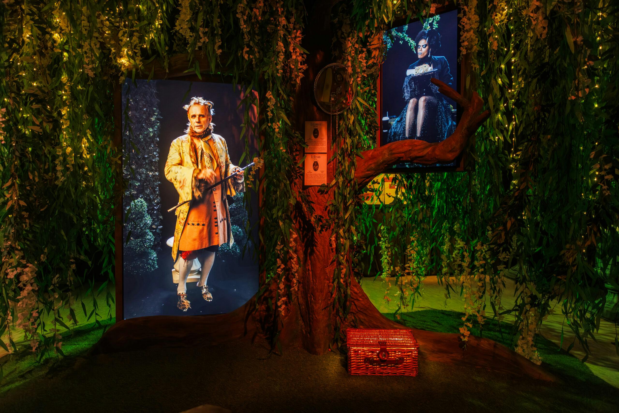 A figure dressed as a character in an orange outfit appears framed by tree branches and foliage in a dimly lit, mystical scene.