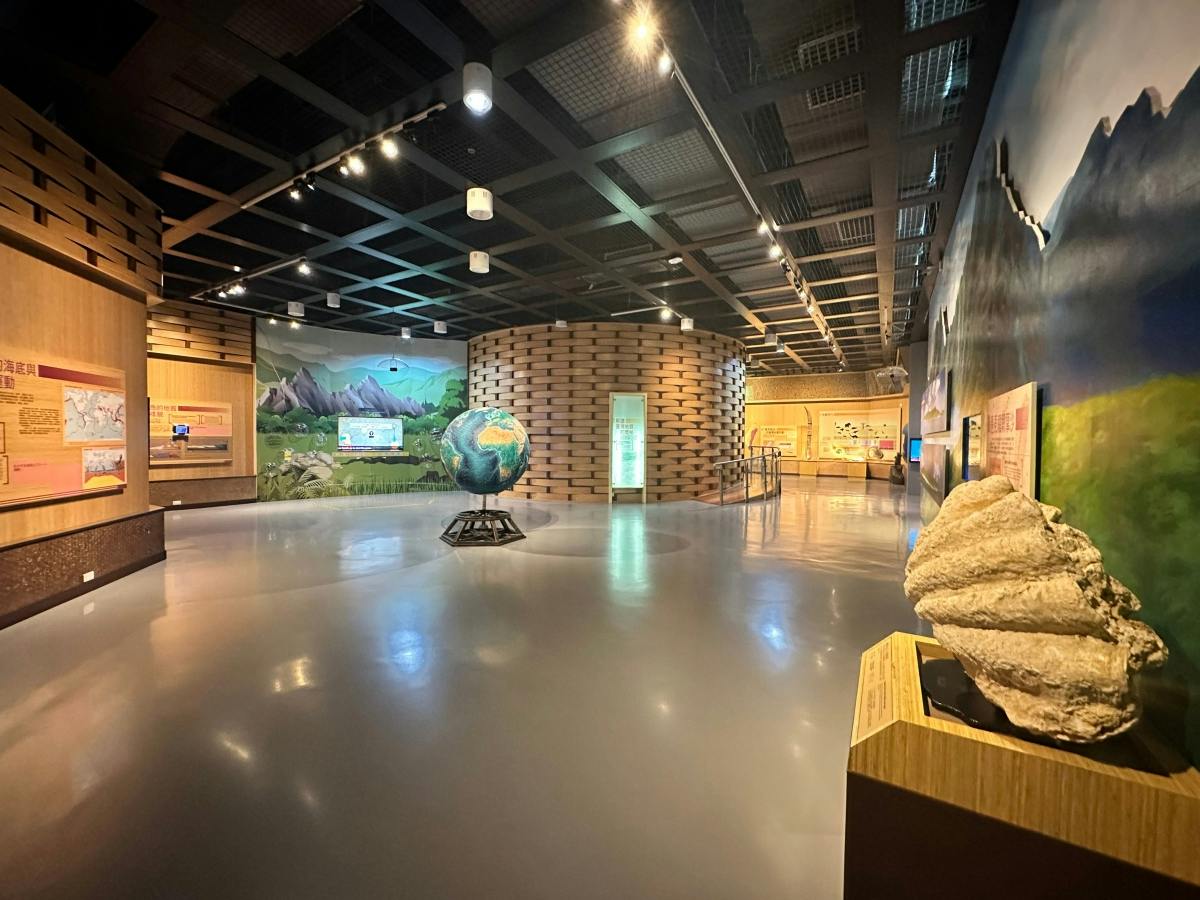 A museum exhibition space with a globe, informational displays, a rock sample, and a cylindrical wooden structure.