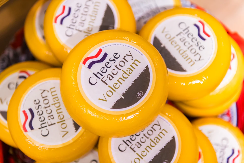 Stacks of yellow cheese rounds labelled "Cheese Factory Volendam" with a logo featuring the Dutch flag.