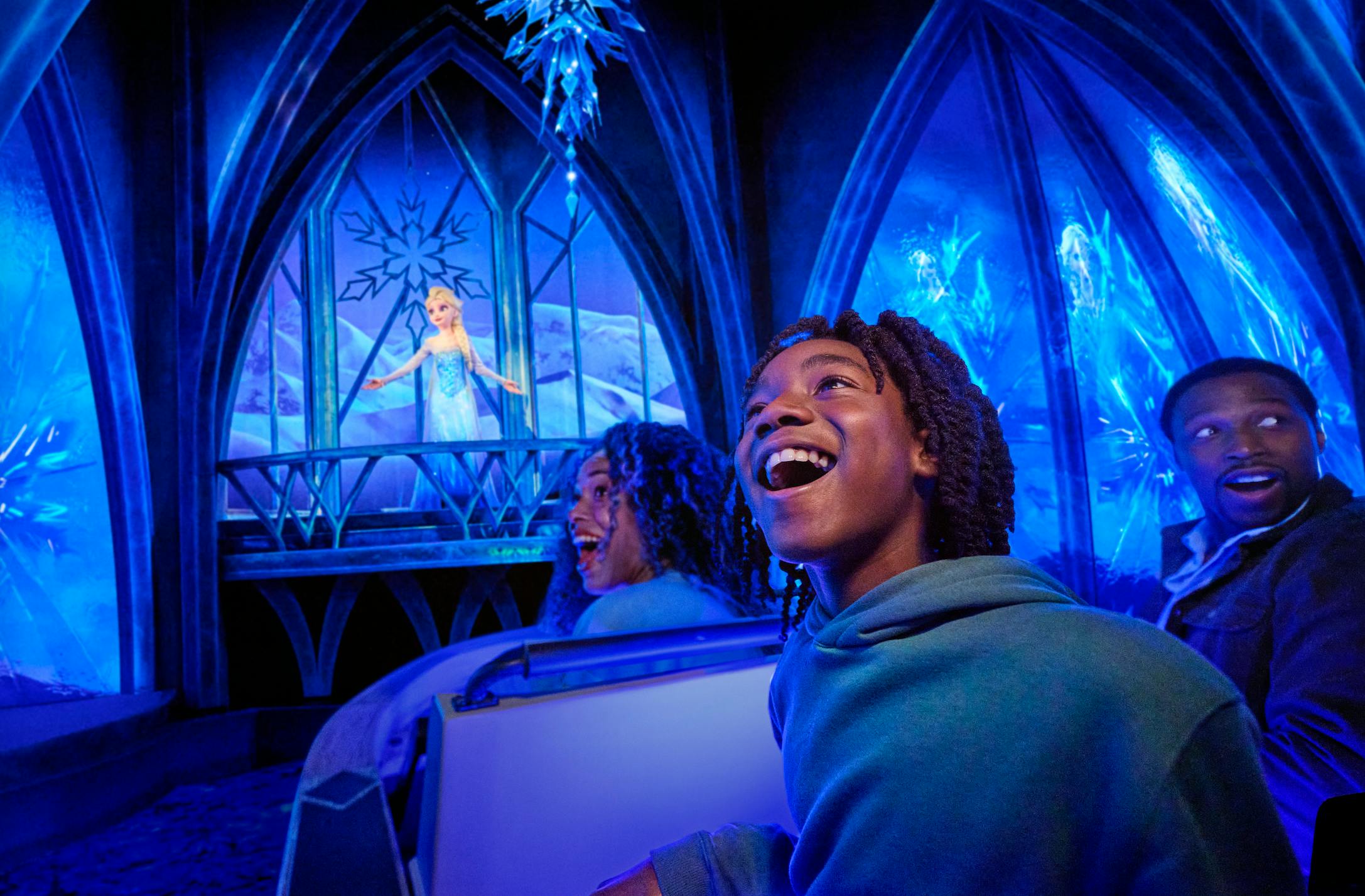 Trzy osoby w przejażdżce z lśniącym niebieskim wnętrzem o lodowatej tematyce, uśmiechające się i rozglądające się podekscytowane.