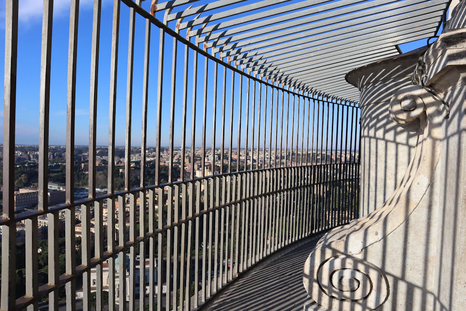 A high vantage point view through vertical metal bars overlooking a cityscape under a clear blue sky.