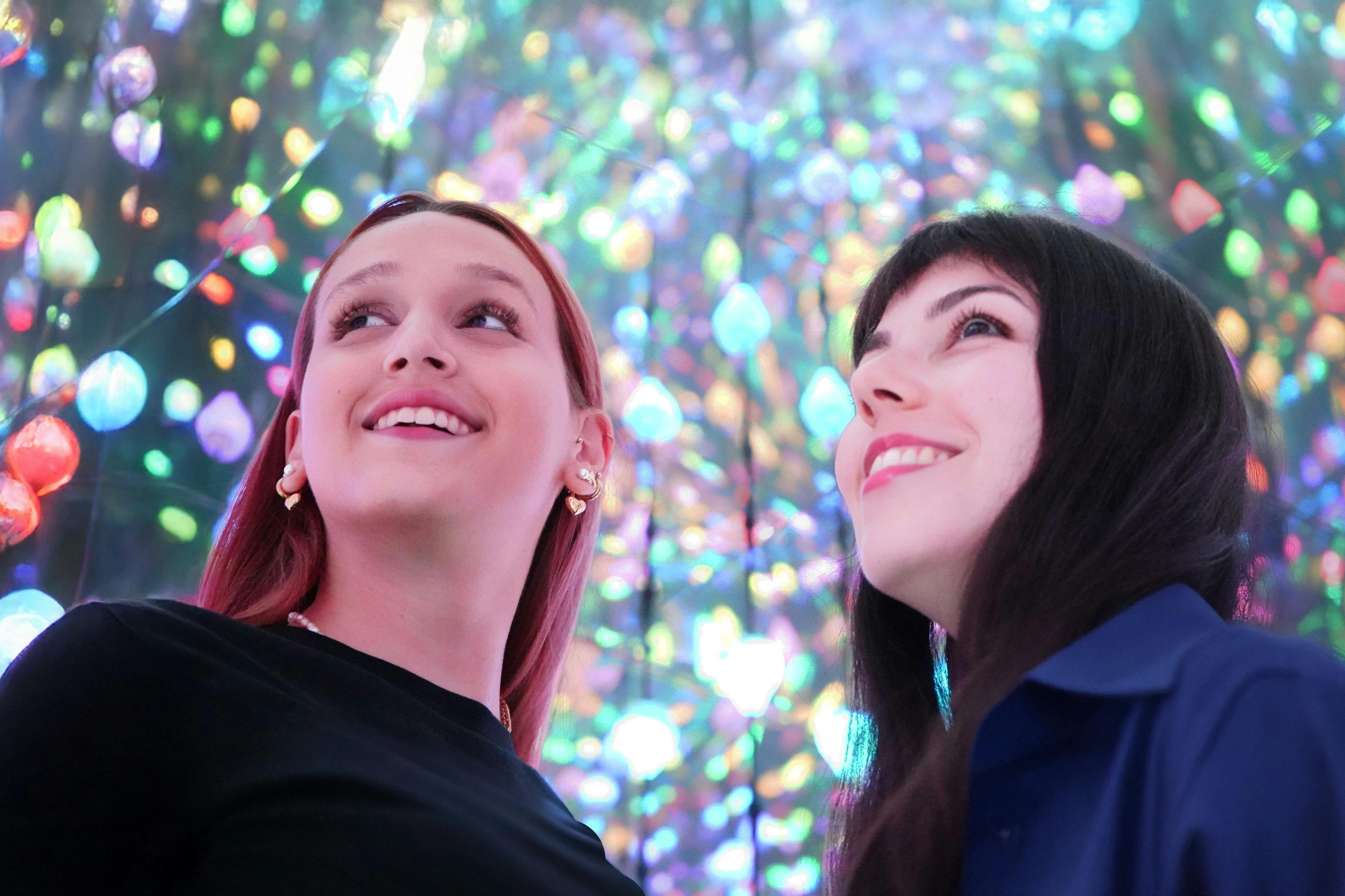 两个人微笑着抬头看着一个五彩缤纷、发光的灯光显示屏，背景中有散景效果。