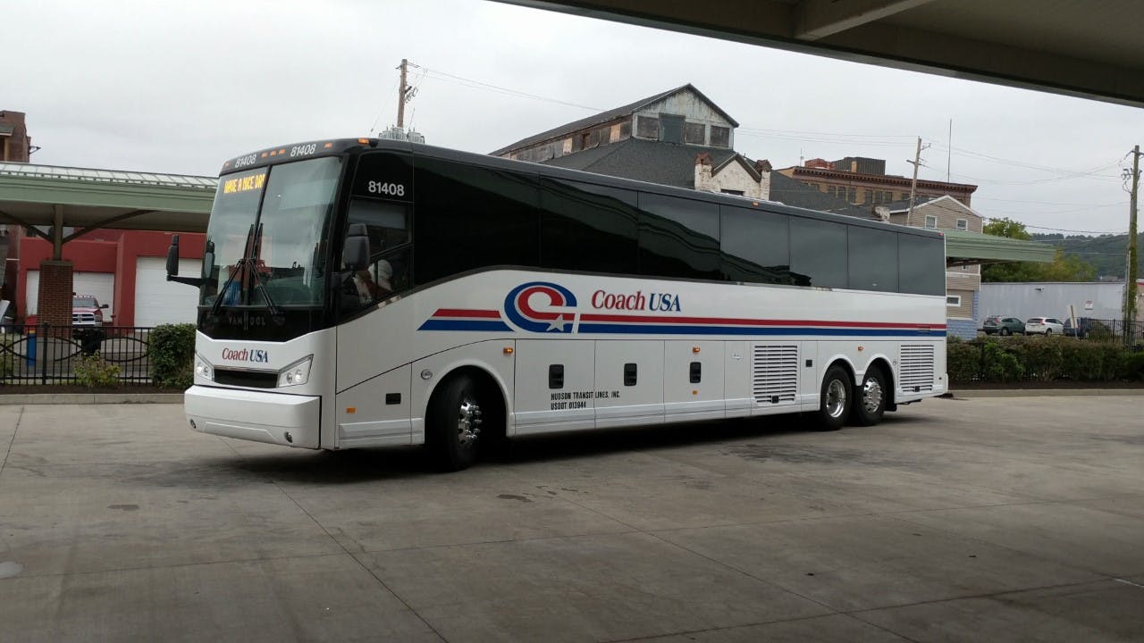 A parked Coach USA bus in a concrete lot with industrial buildings in the background.