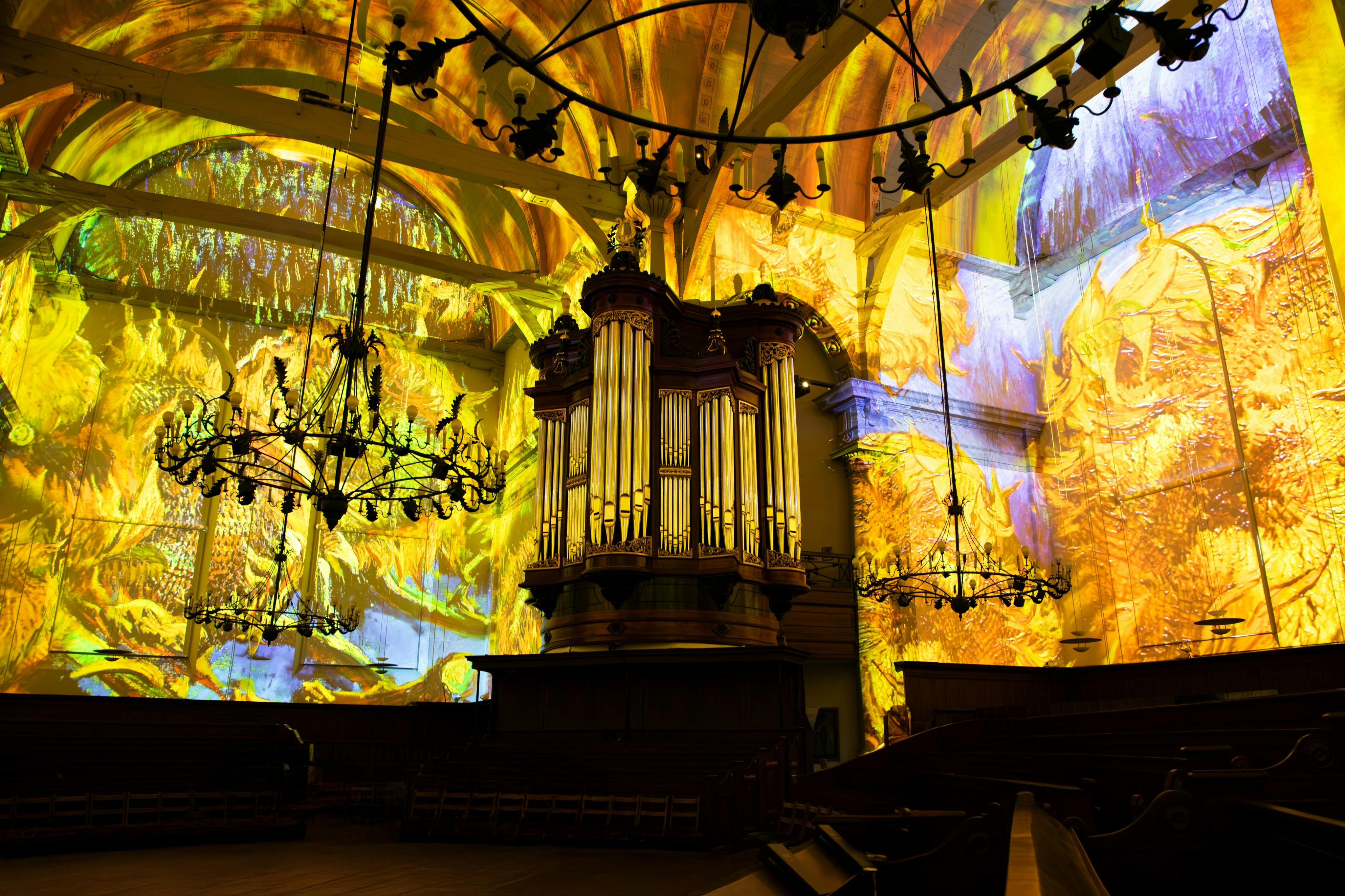 照らされたオルガンを備えた壮大な教会の内部。 カラフルで抽象的な光の投影が壁や天井を覆っています。