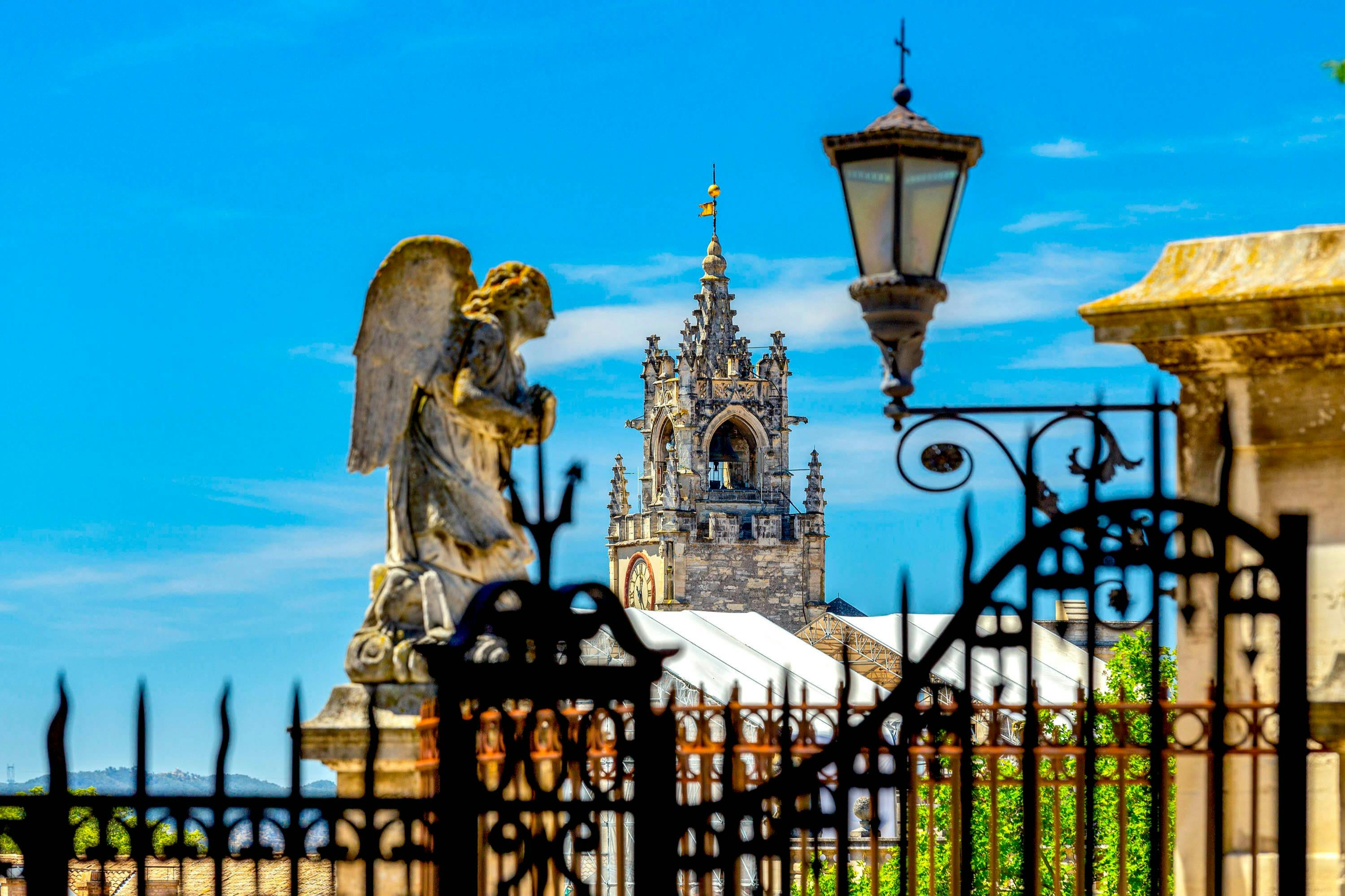 Stone angel statue, ornate iron fence, and Gothic church tower under a blue sky with scattered clouds.